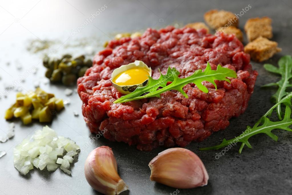 Beef tartare served with an egg yolk on a grey surface, close up