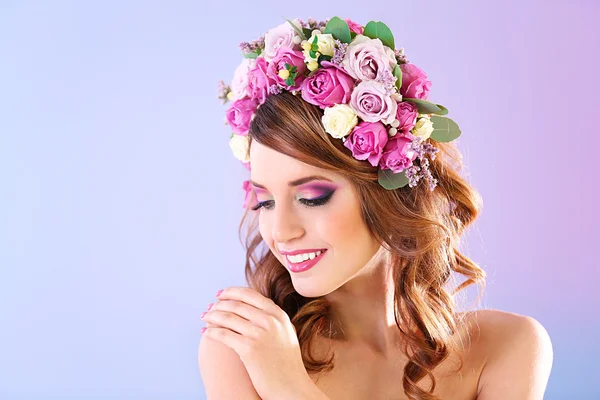Bella giovane donna che indossa fascia floreale su uno sfondo viola — Foto Stock
