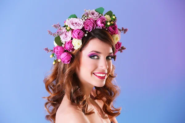 Krásná mladá žena nosí květinová čelenka na fialovém pozadí — Stock fotografie