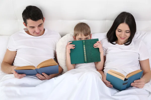 Family reading books in bed at home