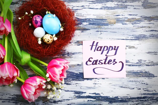 Easter eggs in wicker nest with tulips — Stock Photo, Image