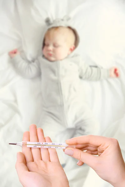 Sovande bebis och hand med termometer — Stockfoto