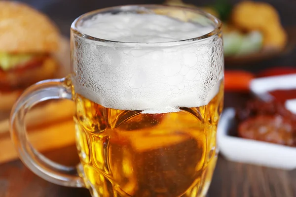 Glass mug of light beer with snacks on dark wooden table, close up — Stock Photo, Image