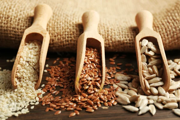 Sésamo, linho e sementes de girassol em colheres de madeira na mesa, close-up — Fotografia de Stock