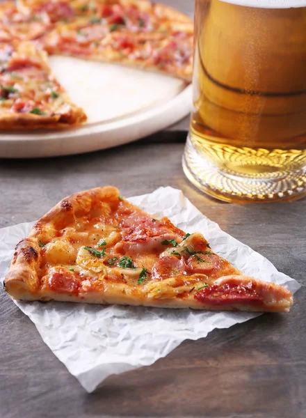 Piece of tasty pizza and glass of beer are on wooden table, close up — Stock Photo, Image