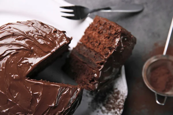 Шоколадный торт на тарелке с разрезанным кусочком и вилкой и какао на сером фоне, крупным планом — стоковое фото
