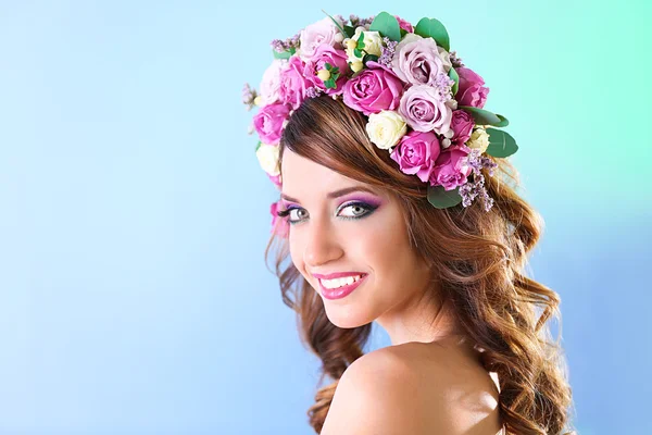 Krásná mladá žena nosí květinová čelenka na modrém pozadí — Stock fotografie