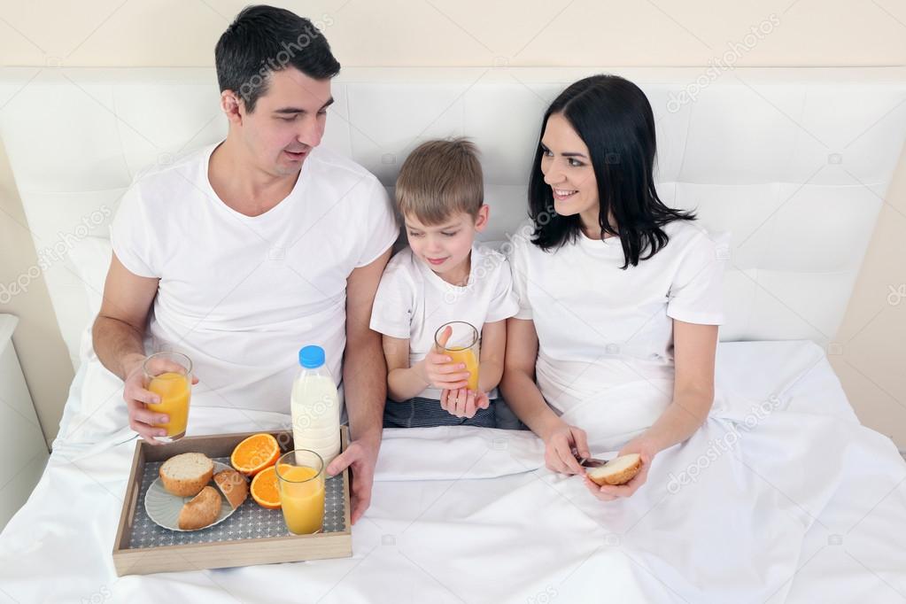 Family having breakfast with orange juice and buns in bed