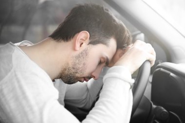 Tired young man asleep in car. clipart
