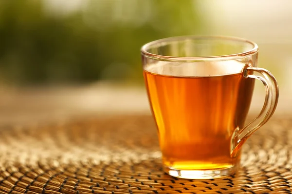 Glass cup of tea on wicker mat against blurred background — Stock Photo, Image