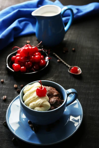 Bolo de chocolate em uma caneca azul com uma cereja em um fundo escuro, close up — Fotografia de Stock