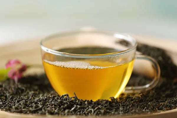 Glass cup of green tea with leaves on wooden plate closeup — Stock Photo, Image