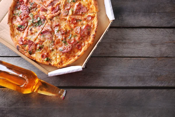 Tasty pizza in carton and bottle of beer are on wooden table, close up