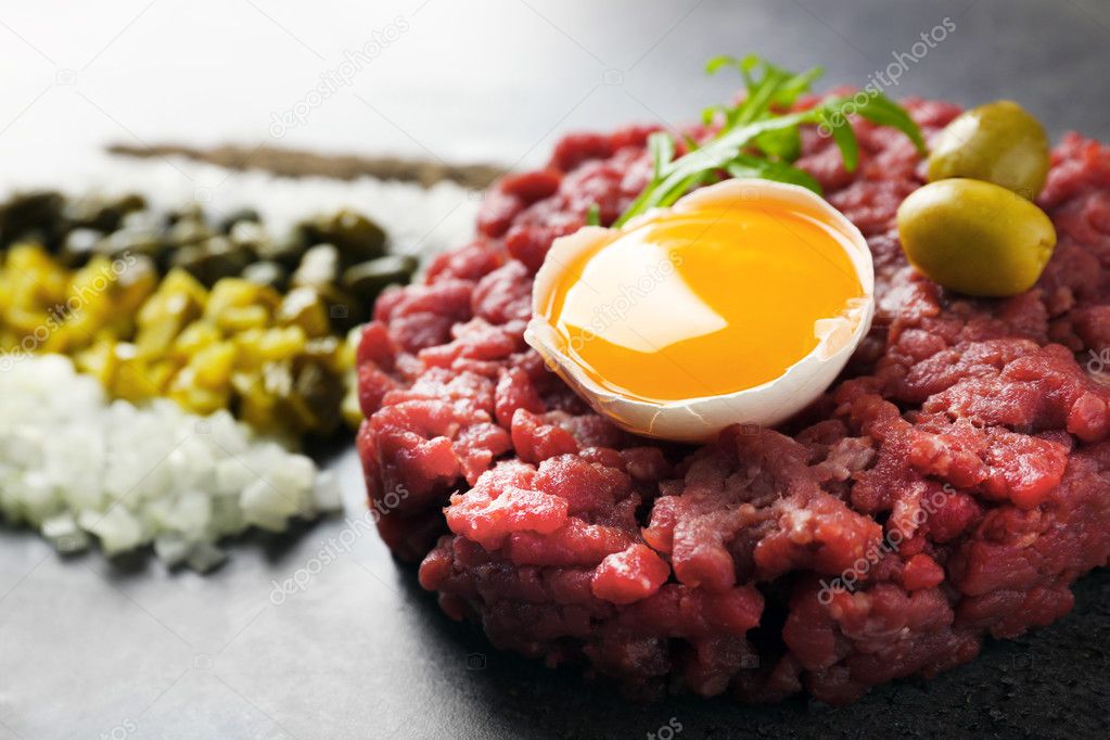Beef tartare served with a set of ingredients on a grey surface, close up