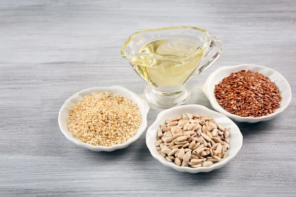 Different kinds of seeds with oil on wooden table — Stock Photo, Image