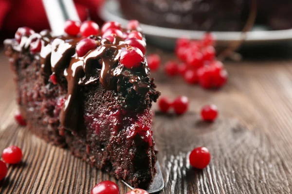 Piece of chocolate cake with cranberries on shovel on wooden table, closeup — Stock Photo, Image