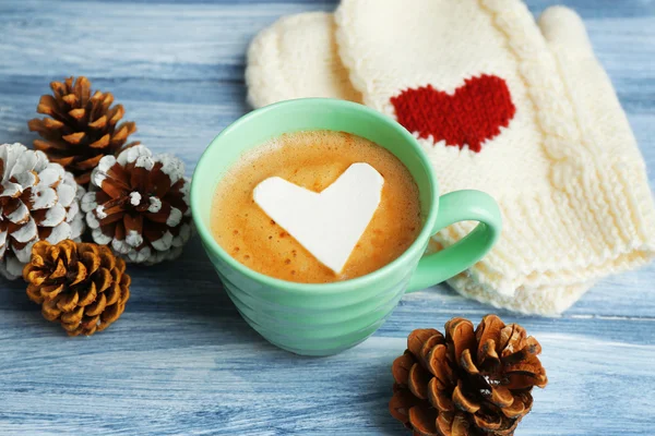 Copa de capuchino caliente con malvavisco del corazón, manoplas calientes y conos de pino sobre fondo de madera azul, de cerca — Foto de Stock