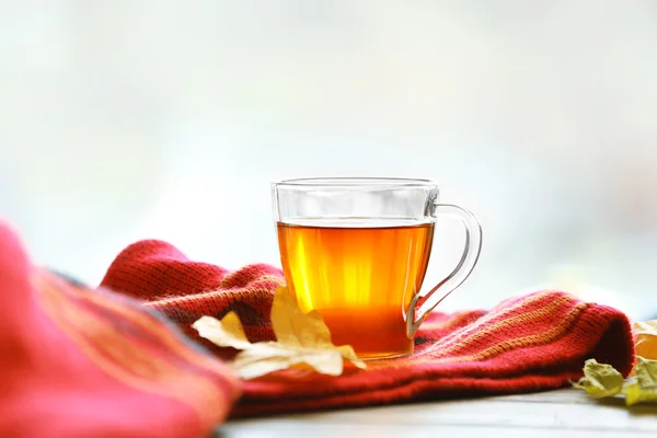 Скляна чашка чаю з червоною пледю та осіннім листям на дерев'яному столі — стокове фото