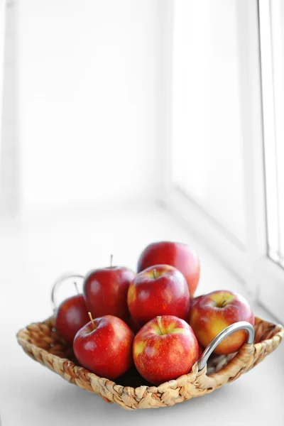 Спелые красные яблоки в плетеной корзине на подоконнике — стоковое фото