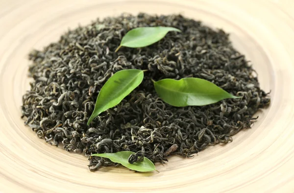 Dry tea with green leaves in beige plate, closeup — Stock Photo, Image