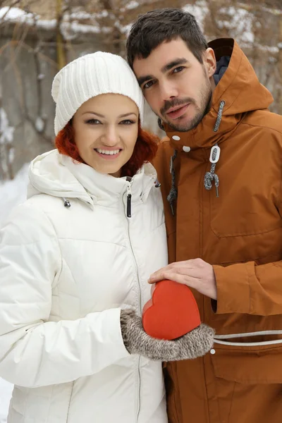 Jovem casal apaixonado segurando coração vermelho no inverno ao ar livre no inverno — Fotografia de Stock