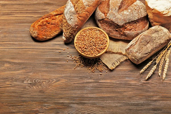 Świeżo pieczony chleb i miskę ziarna pszenicy na drewniane tła — Zdjęcie stockowe