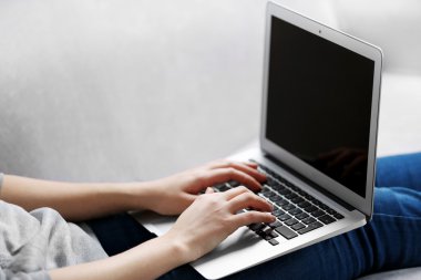 Kanepede dizüstü bilgisayarlı bir kadın oturuyor. 