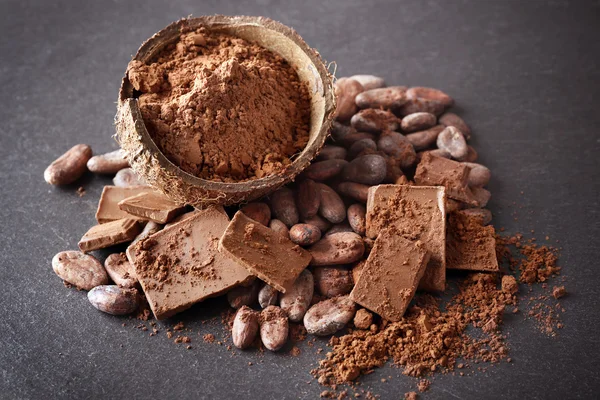 Tigela com grãos de cacau aromáticos e chocolate em fundo cinza, close-up — Fotografia de Stock