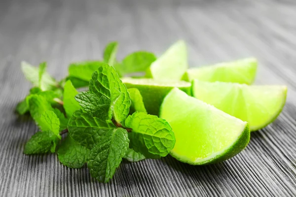 Slices of lime and mint on wooden background — Stock Photo, Image