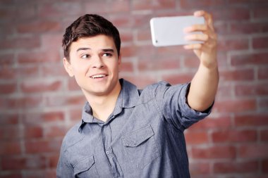 Yakışıklı delikanlı yanında onun kendi cep telefonu ile fotoğraf üzerinde tuğla duvar arka plan yapma