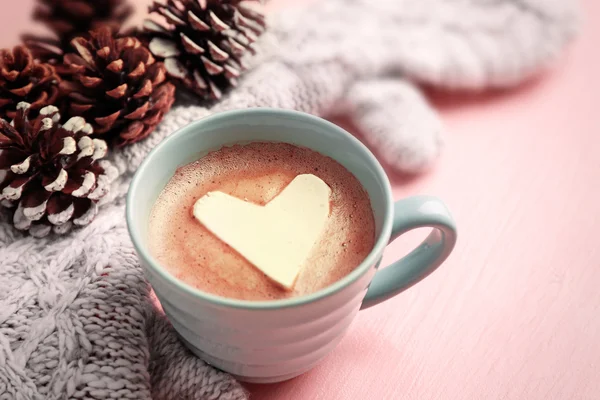 Cup of hot cappuccino with heart marshmallow, warm mittens and pine cones on pink background — Stock Photo, Image