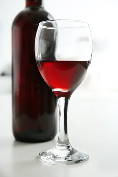 Glass of red wine with bottle on blurred interior background — Stock Photo, Image