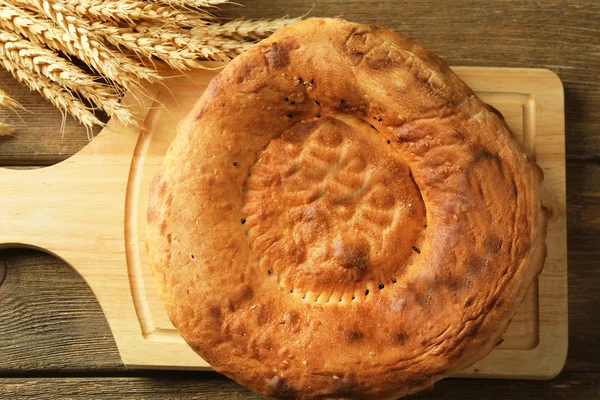 Flat bread and wheat ears on a wooden cutting board, top view — Stock Photo, Image