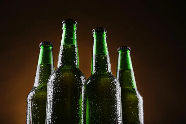 Quattro bottiglie di birra di vetro verde su sfondo scuro illuminato, primo piano — Foto Stock