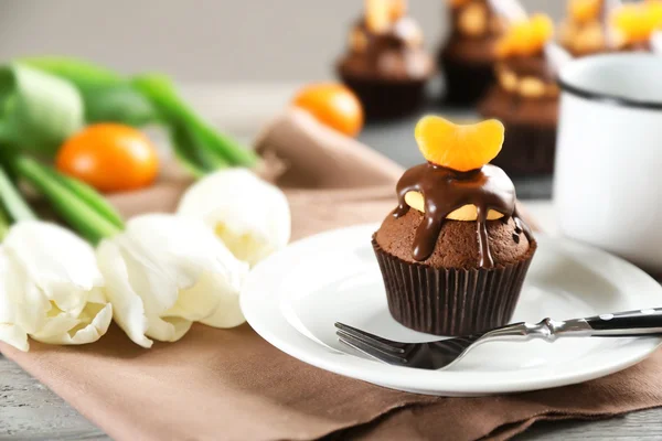 Sabroso cupcake con rebanada de mandarina y chocolate en un plato sobre fondo de madera clara —  Fotos de Stock