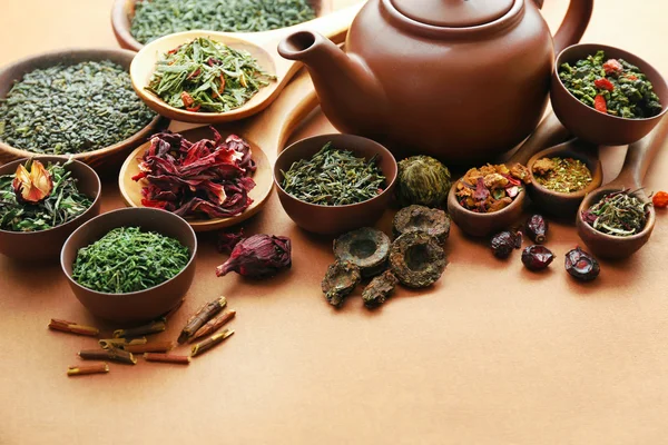 Vielzahl von trockenem Tee in Schalen mit Teekanne auf hellbraunem Hintergrund, Nahaufnahme — Stockfoto