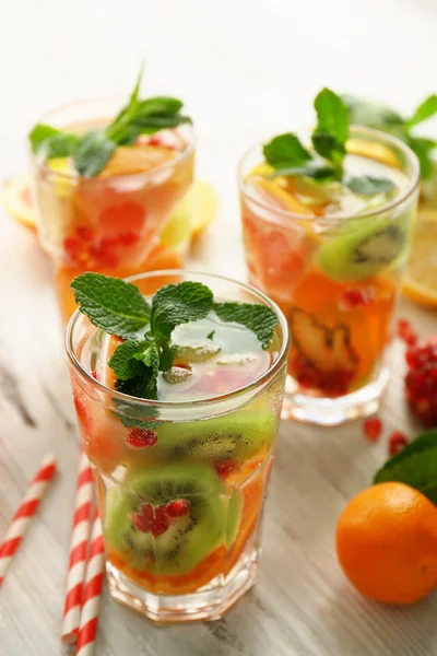 Cocktail rinfrescanti con ghiaccio, menta, semi di melograno e fette di frutta su fondo di legno chiaro — Foto Stock