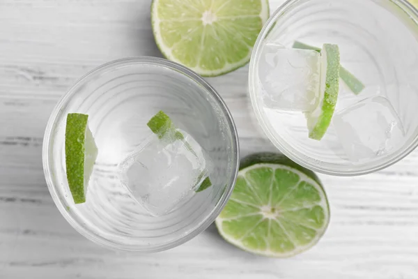 Fresh cocktails with ice and lime on white wooden table background, view from above — Stock Photo, Image