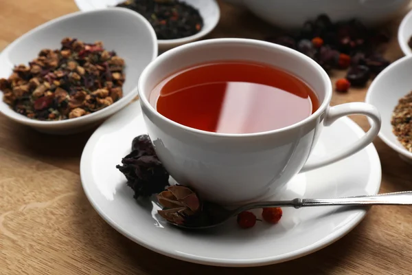 Tea concept. Cup of tea with teapot and different kinds of dry tea on wooden table, close up — Stock Photo, Image