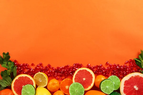 Zitrusfrüchte mit Granatapfelkernen auf orangefarbenem Hintergrund — Stockfoto