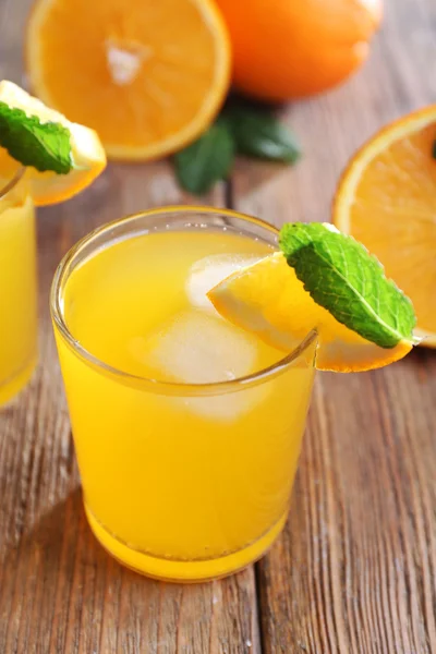 Два апельсиновых сока со льдом и апельсином на фоне стола — стоковое фото