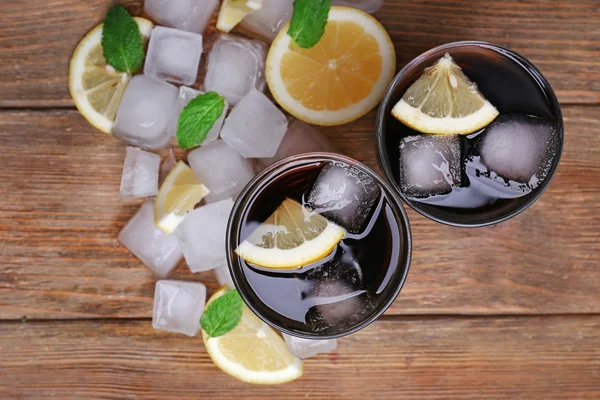 Dois copos de cola com cubos de gelo e limão sobre fundo de mesa de madeira — Fotografia de Stock