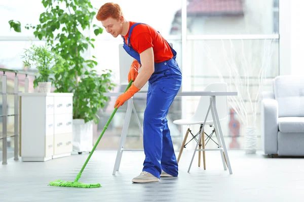 Young janitor with brush cleaning floor — Stock Photo, Image