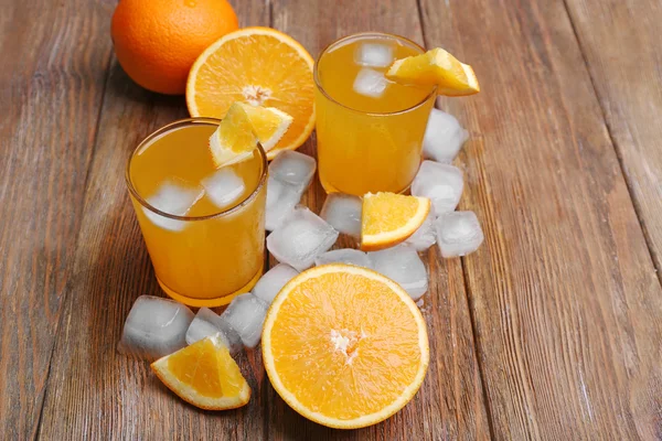 Two orange juices with cubes of ice and orange on wooden table background — Stock Photo, Image