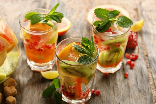 Cocktail rinfrescanti con ghiaccio, menta, semi di melograno e fette di frutta su fondo rustico in legno — Foto Stock