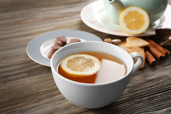 杯自酿茶，柠檬和木制的桌子上的糖果 — 图库照片