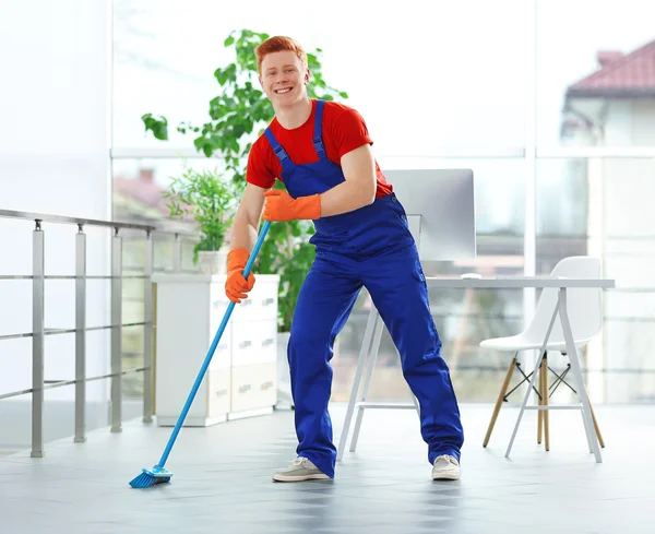 Young janitor with brush cleaning floor — Stock Photo, Image