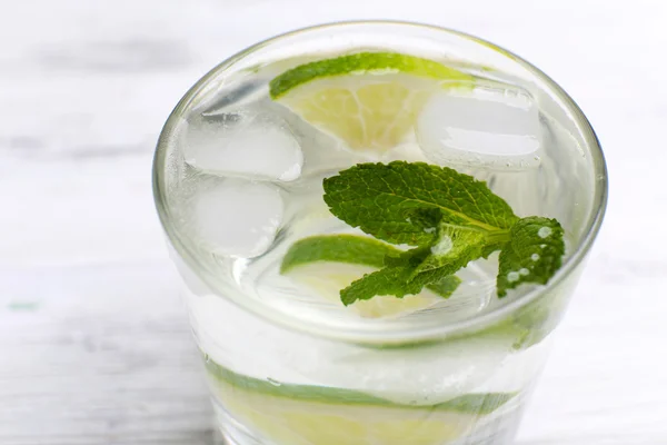 Cóctel fresco con hielo, menta y lima sobre fondo de mesa de madera blanca — Foto de Stock