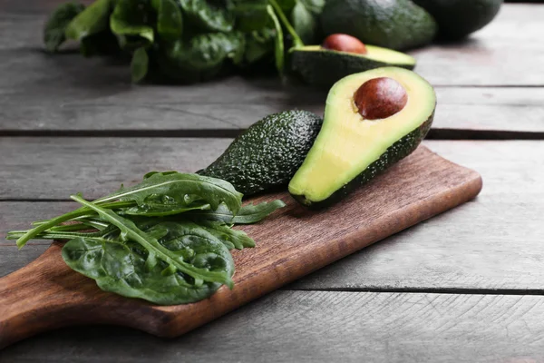 Sliced avocado with spinach and arugula on wooden cutting board — Stock Photo, Image