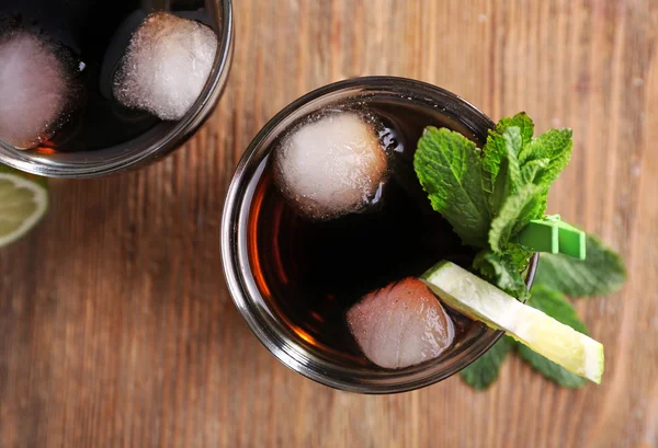 Deux verres de cola avec glace, menthe et citron vert sur fond de table en bois, vue d'en haut — Photo